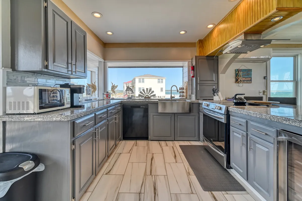 A modern kitchen featuring granite countertops, sleek appliances, and a large window that frames beautiful ocean views. The space feels airy and inviting, ideal for preparing meals or gathering after a day of exploring the local area.