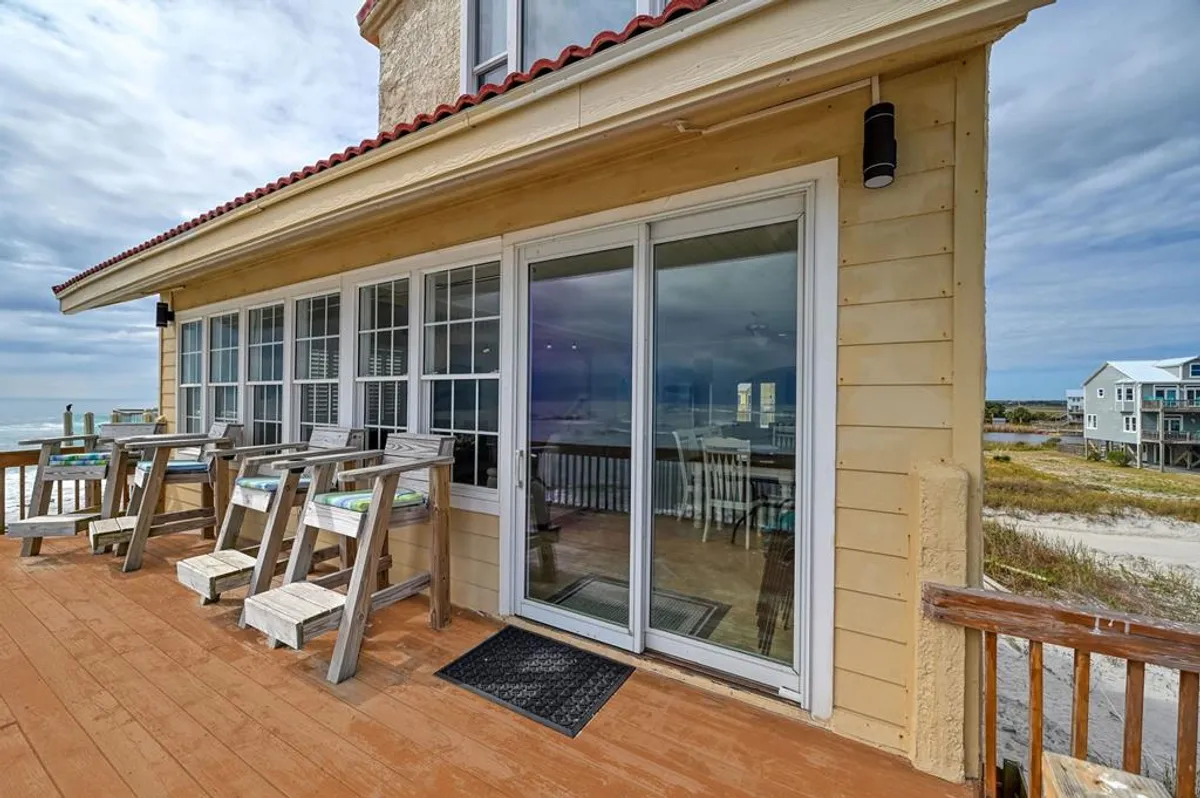 A sun deck overlooking the ocean, featuring comfortable deck seating and a sliding glass door that opens into the great room. The inviting setup encourages alfresco dining, relaxing with a book, or simply soaking in the sea breeze while enjoying the horizon.