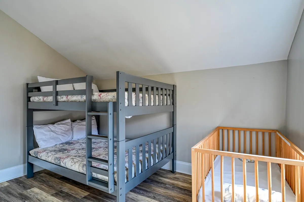 A charming bedroom with a bunk bed and a crib, designed for families with young children. The space feels practical yet welcoming, perfect for both restful sleep and playful mornings.