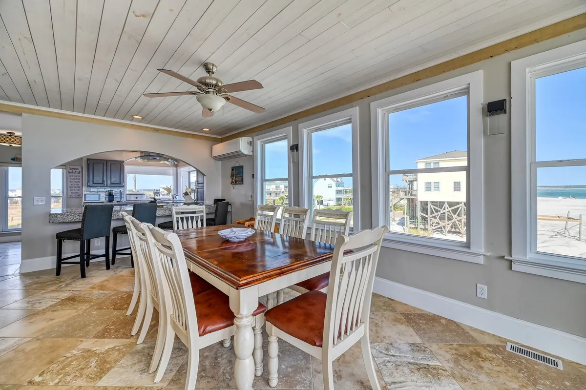 A casual dining area with a large table set beside windows offering sweeping ocean views. The space is flooded with natural light and designed for enjoying meals with family or friends against a scenic backdrop.