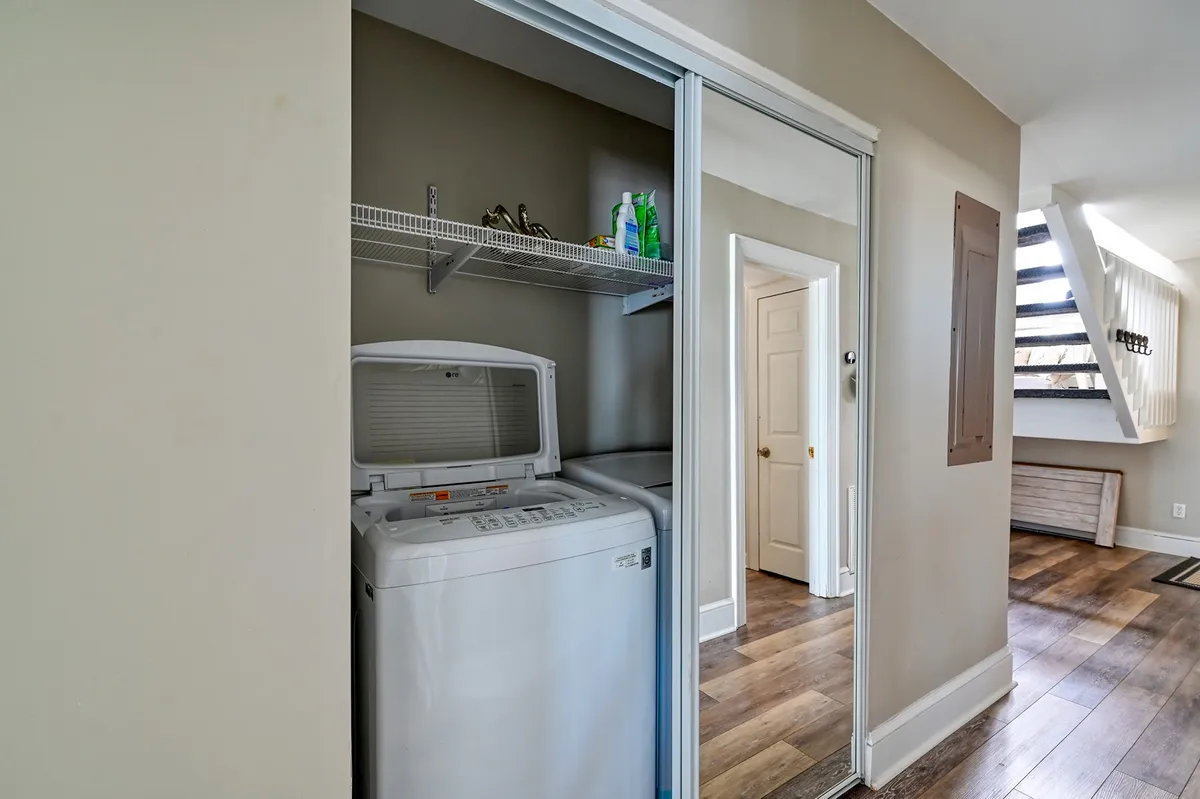 A practical laundry area with a washing machine, shelves stocked with cleaning products, and a doorway leading further into the house, evoking a sense of thoughtful amenities and flexibility for guest needs.