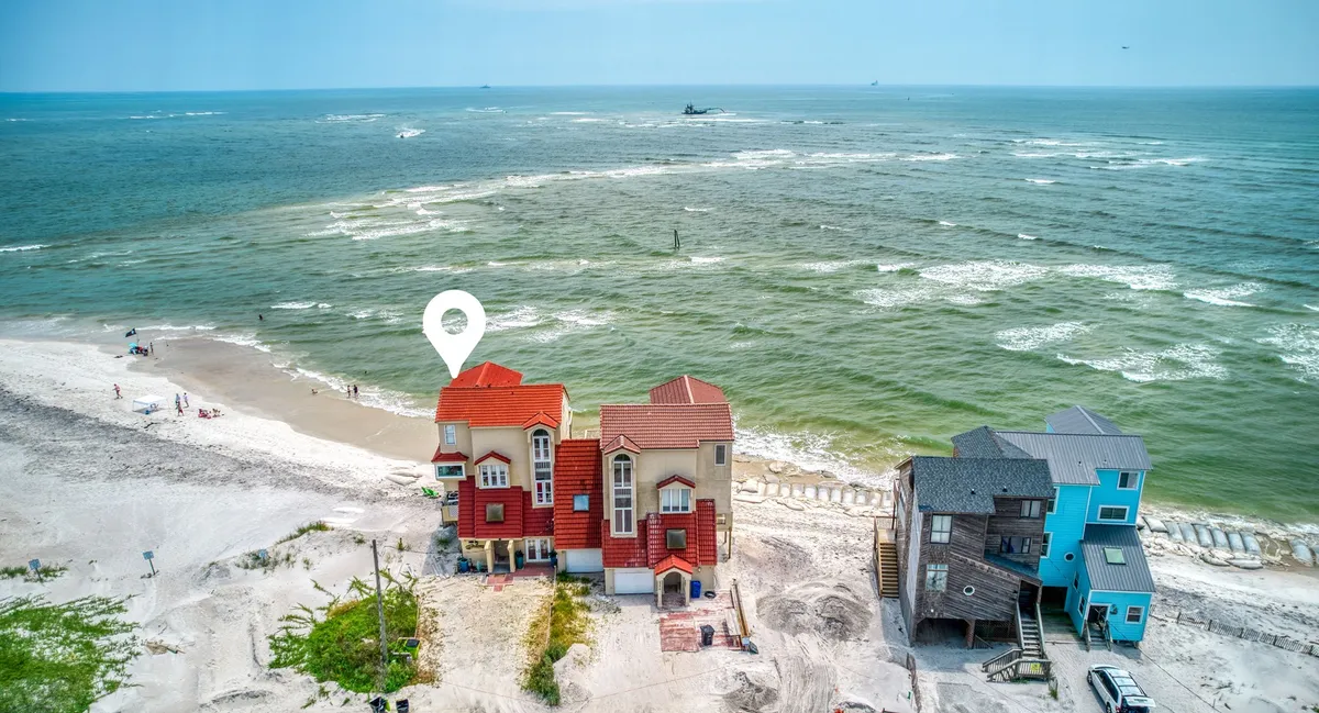 This exterior image captures beachfront houses, gentle ocean waves, and sandy stretches—the direct context for the game room's indoor-outdoor experience. The proximity between the living spaces and the beach is evident, emphasizing easy access for sandy feet and spontaneous outdoor activities.